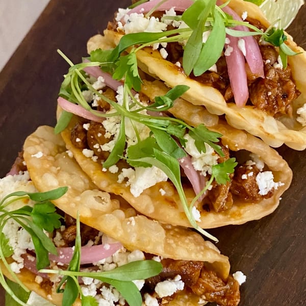 E+O Kitchen's crispy tacos filled with meat, topped with pickled onions, crumbled cheese, and microgreens.