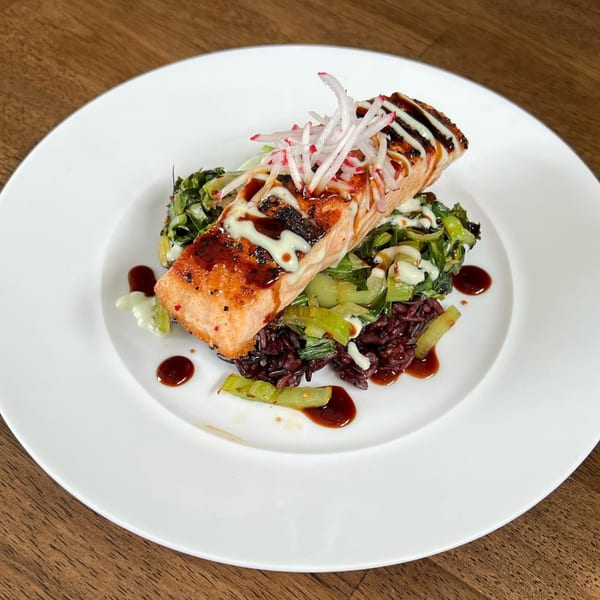 E+O Kitchen's salmon dish with black rice, green vegetables, and radish on a white plate.