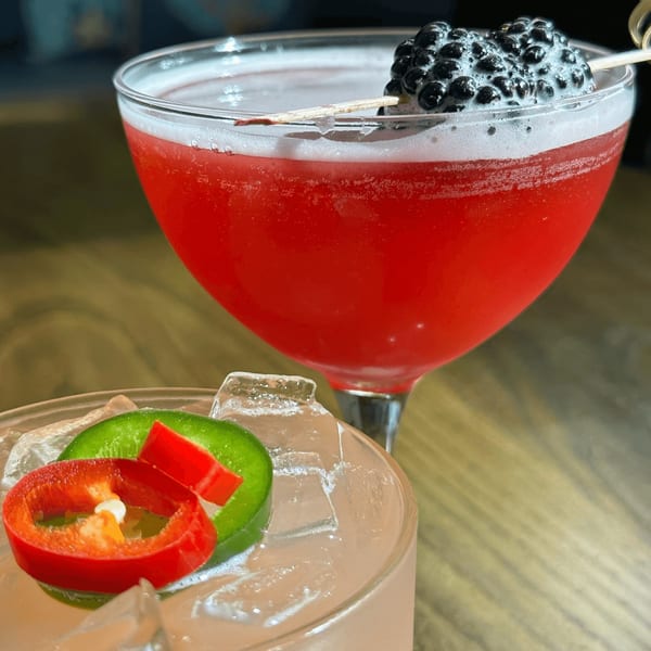 Two E+O Kitchen cocktails: a red drink with blackberries and a clear drink with chili peppers.