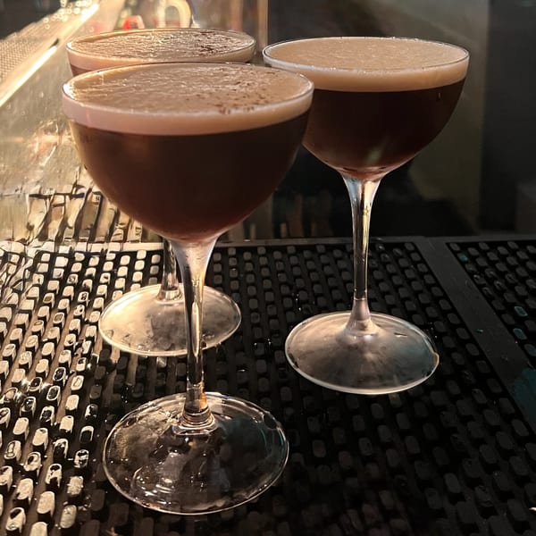 Three espresso martinis with frothy tops sit on a bar mat at E+O Kitchen.