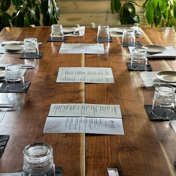 A long wooden dining table at E+O Kitchen set with menus, plates, and glasses.