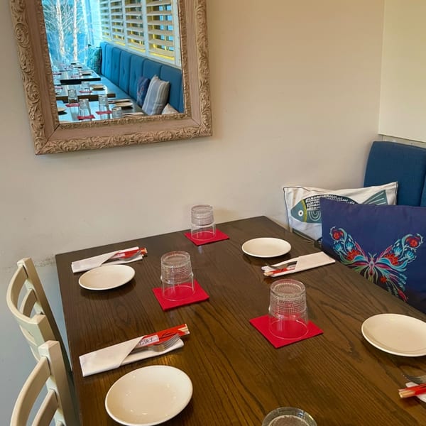 A dining table set with plates, glasses, and chopsticks, reflecting a blue booth in a mirror.
