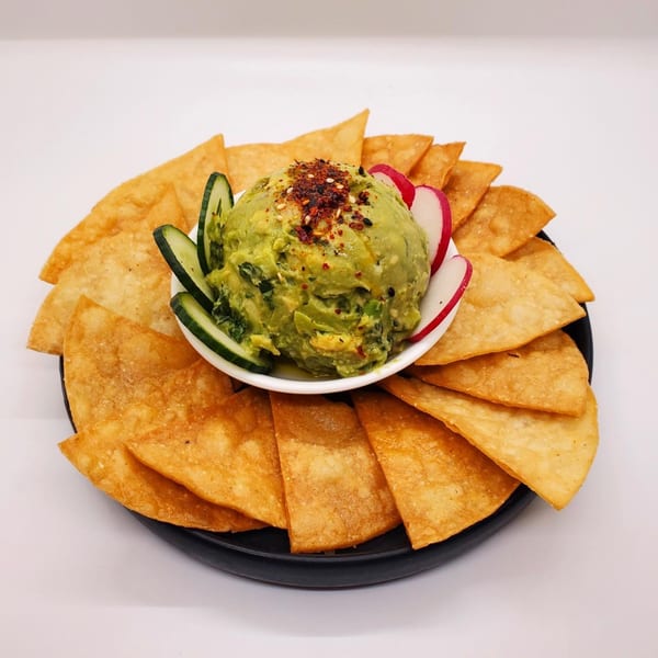 Guacamole topped with chili flakes and sesame seeds, served with tortilla chips, cucumber, and radish.