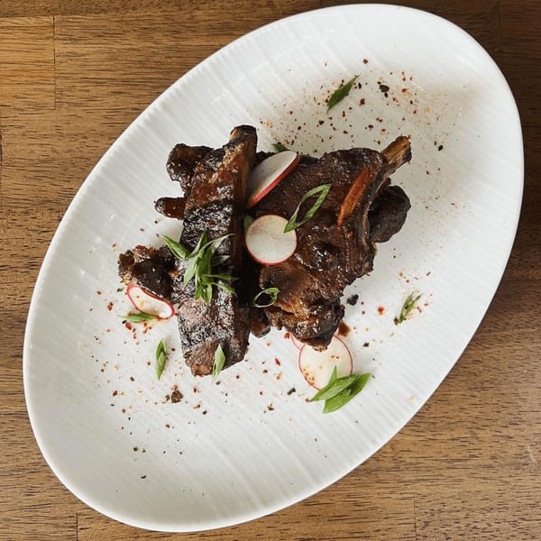 E+O Kitchen's Asian-fusion ribs, garnished with sliced radishes and green onions on a white plate.