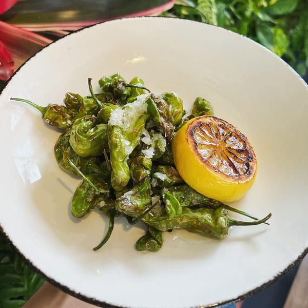 E+O Kitchen's blistered shishito peppers with flaky salt and a grilled lemon half on a white plate.