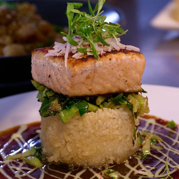 Seared salmon with greens and shredded radish atop rice, drizzled with sauce at E+O Kitchen.