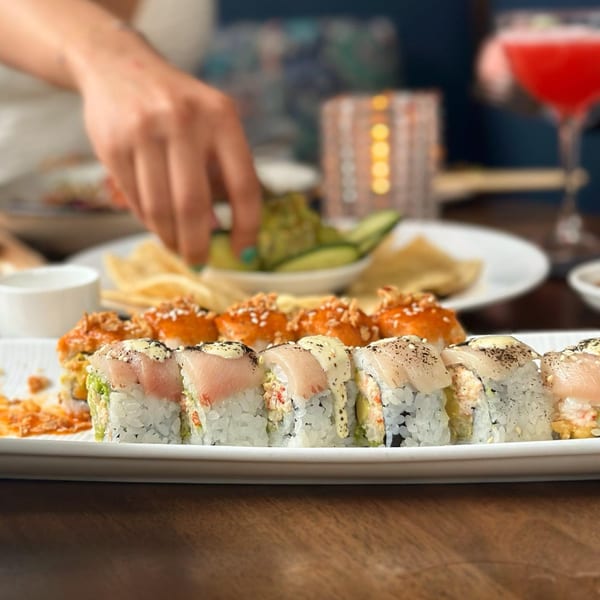 A plate of sushi rolls with a person's hand reaching for food in the background at E+O Kitchen.