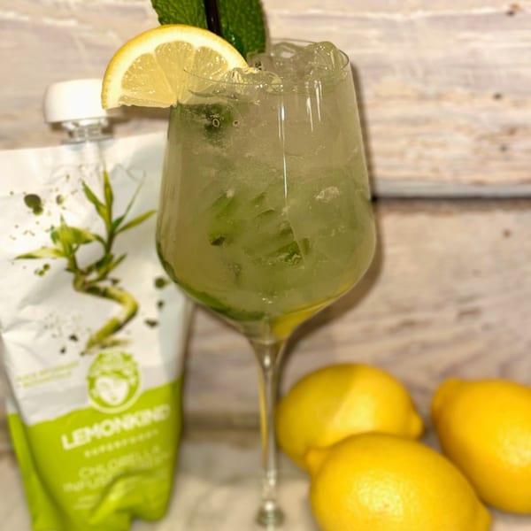 Green cocktail with lemon slice and mint, next to lemons and a Lemonkind pouch.