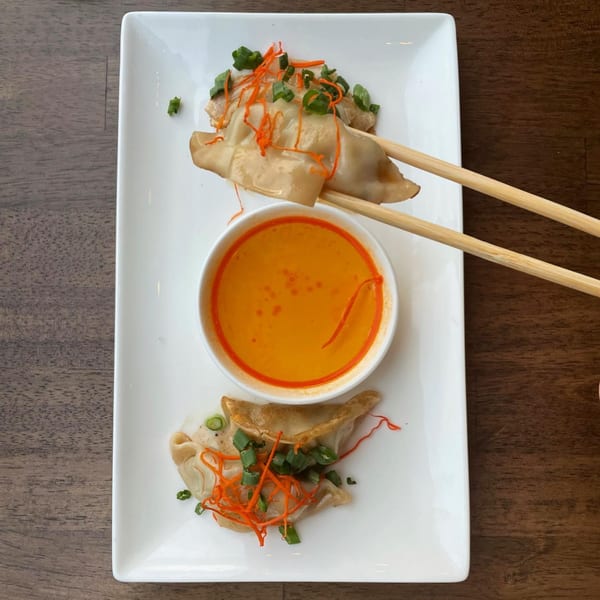 E+O Kitchen's pan-fried dumplings with shredded carrots and scallions, served with a dipping sauce.