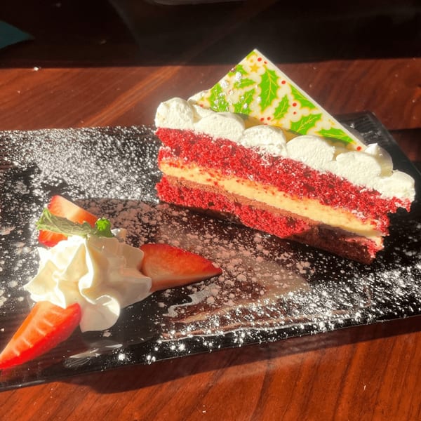 Red velvet cake slice with whipped cream, strawberries, and a festive holly chocolate garnish.