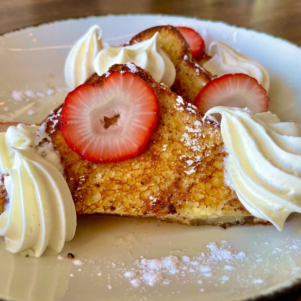 Golden French toast triangles topped with whipped cream, sliced strawberries, and powdered sugar.