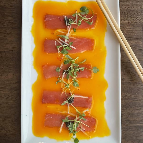 E+O Kitchen's tuna sashimi with orange sauce, microgreens, and chopsticks on a white plate.