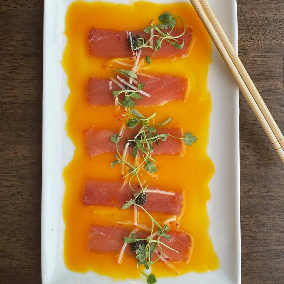 E+O Kitchen's tuna sashimi with orange sauce, microgreens, and chopsticks on a white plate.