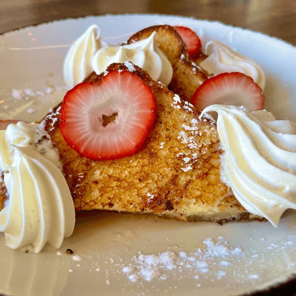Golden French toast topped with whipped cream, sliced strawberries, and powdered sugar.