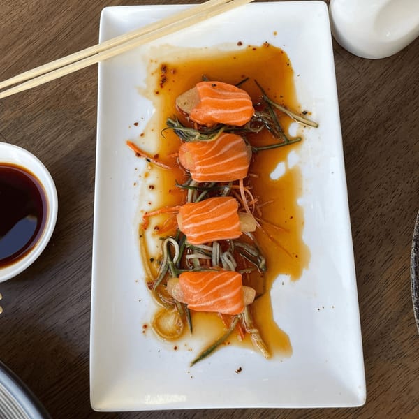 E+O Kitchen's salmon sashimi with vegetables and sauce on a white rectangular plate.