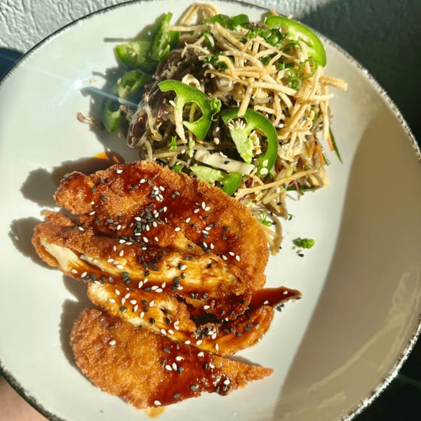 Crispy chicken with sweet sauce and sesame seeds, alongside a noodle and vegetable salad with jalapeños.