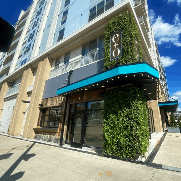 Exterior of E+O Kitchen, an asian-fusion restaurant, with a vibrant green ivy-covered wall and bright blue awning.