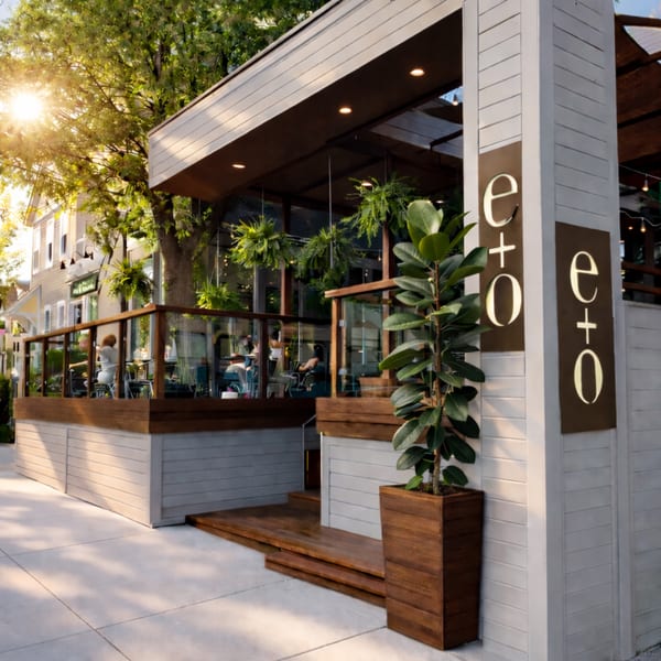 Exterior of E+O Kitchen, a modern restaurant with a sunny outdoor patio and lush greenery.