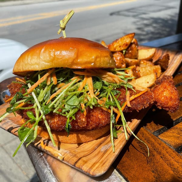 E+O Kitchen's crispy chicken sandwich with greens, carrots, and a side of potato wedges.